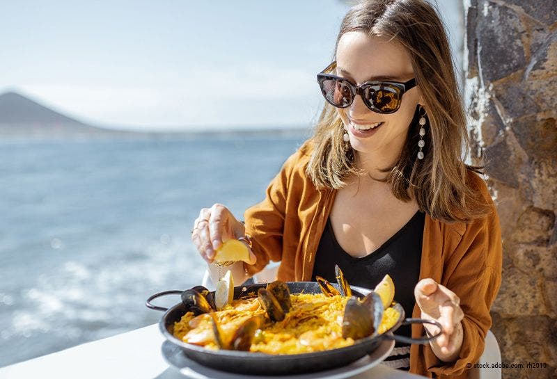 Frau am Meer isst Paella